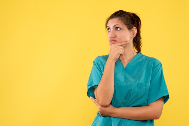 Vista frontal doctora en camisa médica pensando en fondo amarillo