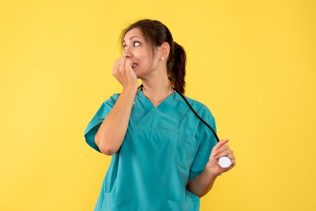 Vista frontal doctora en camisa médica que se siente nerviosa sobre fondo amarillo