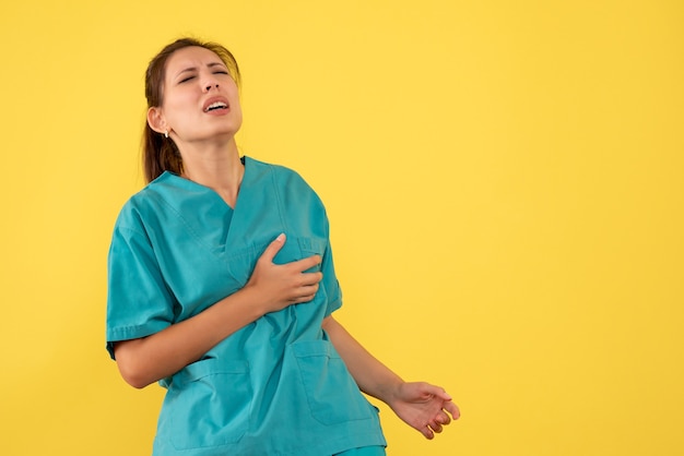 Vista frontal doctora en camisa médica que sufre de dolor de corazón sobre fondo amarillo