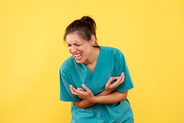 Vista frontal doctora en camisa médica que sufre de dolor sobre fondo amarillo