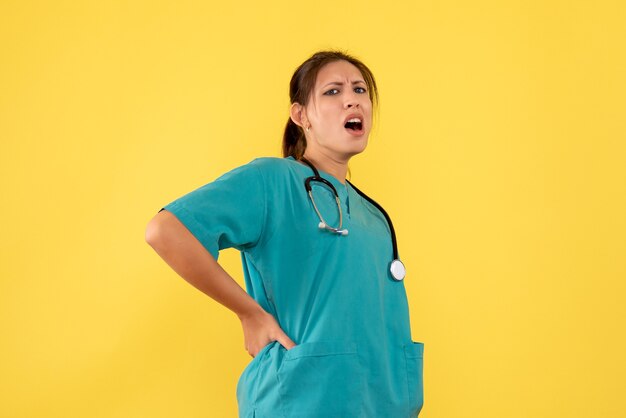 Vista frontal de la doctora en camisa médica que tiene algo de dolor sobre fondo amarillo