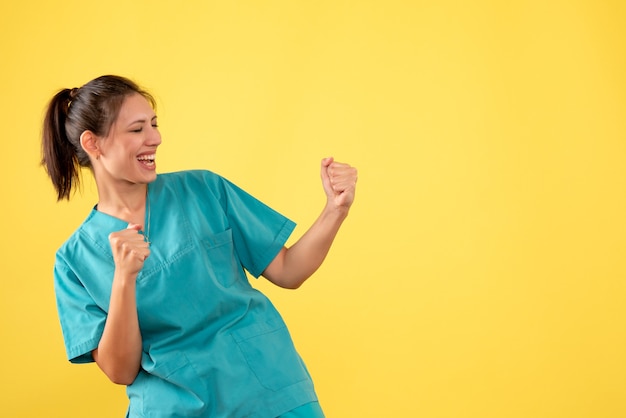 Vista frontal doctora en camisa médica regocijándose sobre fondo amarillo