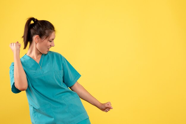 Vista frontal doctora en camisa médica regocijándose sobre fondo amarillo