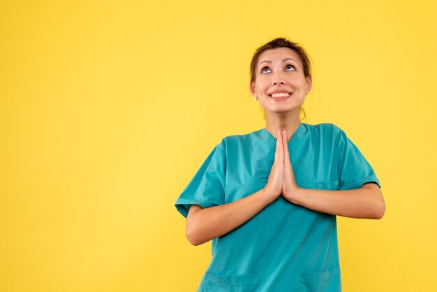 Vista frontal doctora en camisa médica rezando sobre fondo amarillo