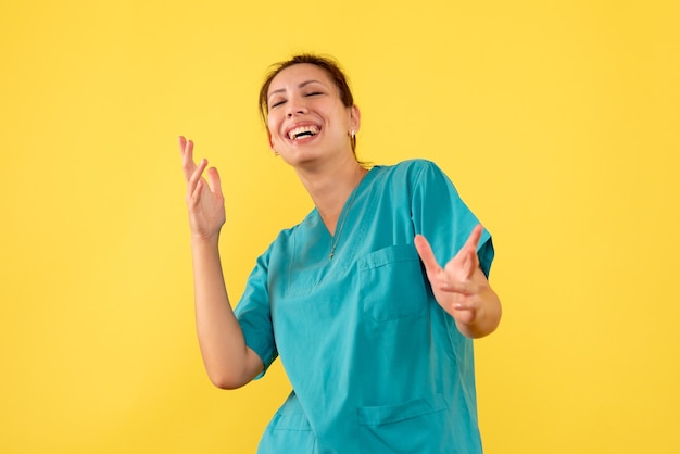 Vista frontal doctora en camisa médica riendo sobre fondo amarillo