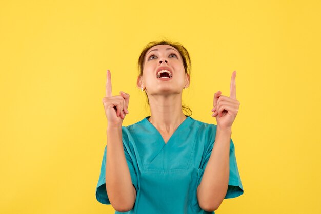 Vista frontal doctora en camisa médica sobre fondo amarillo