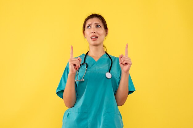 Vista frontal doctora en camisa médica sobre fondo amarillo