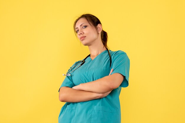 Vista frontal doctora en camisa médica sobre fondo amarillo