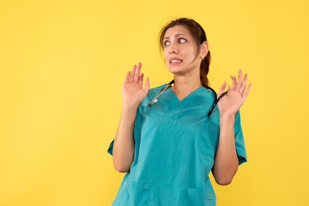 Vista frontal doctora en camisa médica sobre fondo amarillo