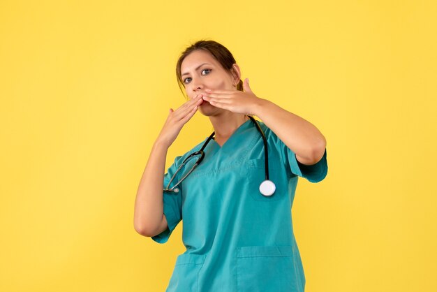 Vista frontal doctora en camisa médica sobre fondo amarillo