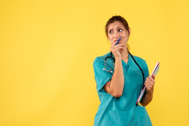 Vista frontal doctora en camisa médica sosteniendo análisis en escritorio amarillo virus salud color covid- emoción médico hospital