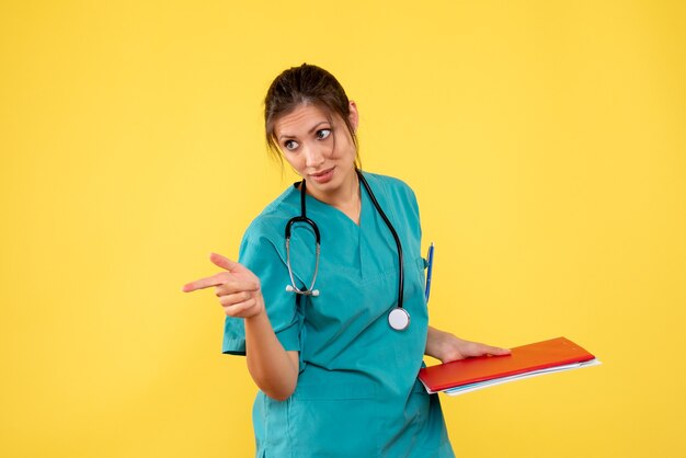 Vista frontal doctora en camisa médica sosteniendo notas sobre fondo amarillo