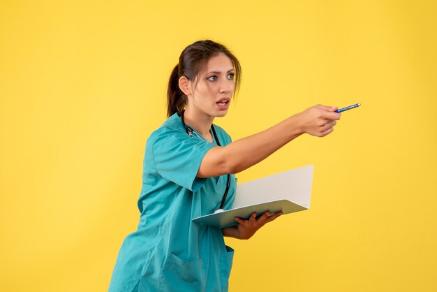 Vista frontal doctora en camisa médica sosteniendo notas sobre fondo amarillo