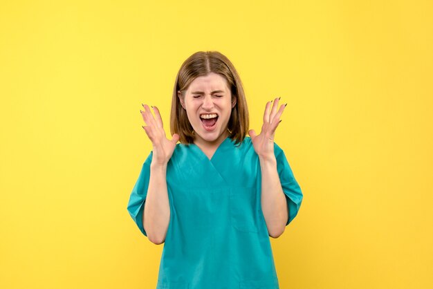 Vista frontal de la doctora con cara gritando en la pared amarilla