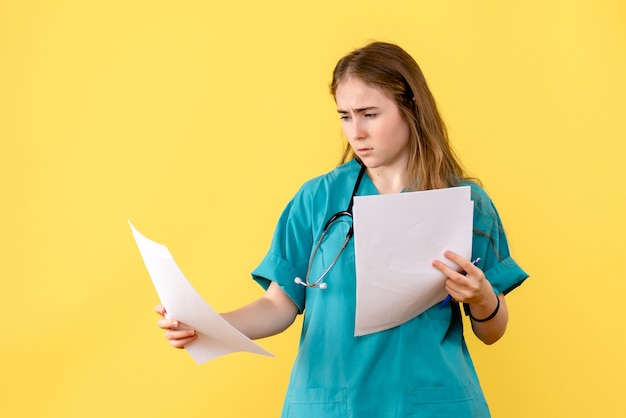 Vista frontal doctora con documentación sobre un fondo amarillo enfermera del hospital de salud