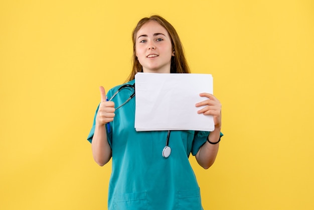 Vista frontal doctora con documentación sobre un fondo amarillo enfermera hospital salud