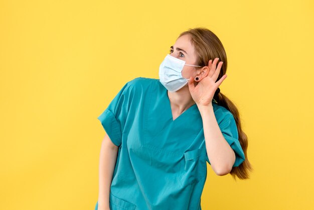 Vista frontal doctora escuchando sobre fondo amarillo hospital de salud covid- pandemia