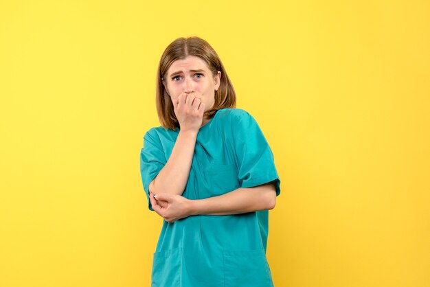 Vista frontal de la doctora con expresión de miedo en la pared amarilla