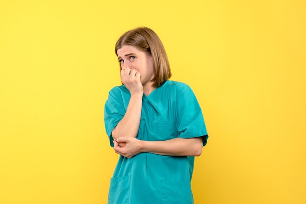 Vista frontal de la doctora con expresión de miedo en la pared amarilla