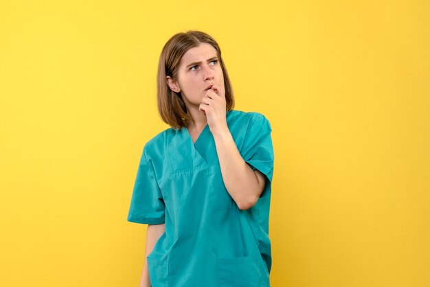 Vista frontal de la doctora con expresión de pensamiento en la pared amarilla