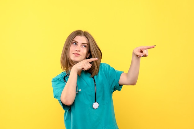 Vista frontal de la doctora con expresión sonriente en la pared amarilla