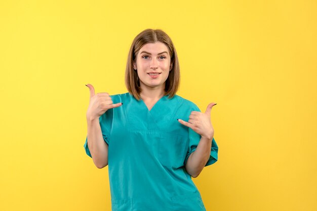 Vista frontal de la doctora con expresión sonriente en la pared amarilla