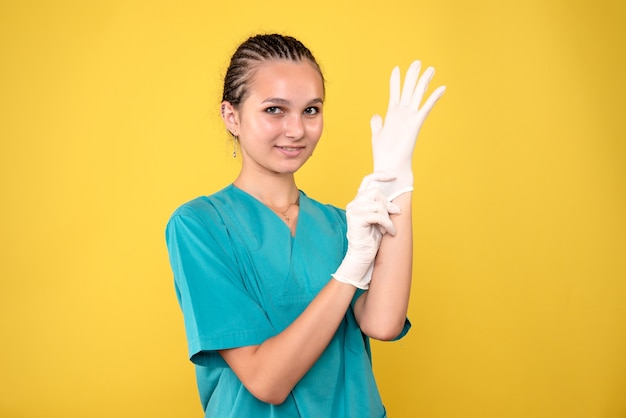 Vista frontal de la doctora con guantes en la pared amarilla