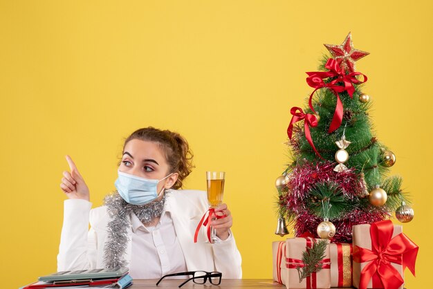 Vista frontal doctora en máscara celebrando la Navidad con champán