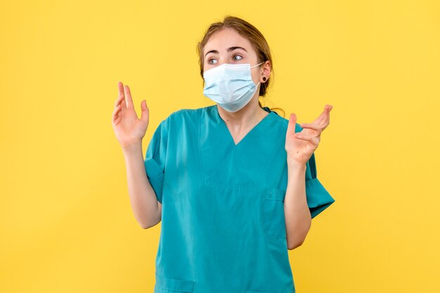 Vista frontal doctora en máscara en escritorio amarillo covid- pandemia de hospital de salud