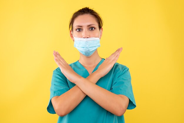 Vista frontal doctora en máscara estéril en escritorio amarillo enfermera virus salud médico hospital enfermedad emoción