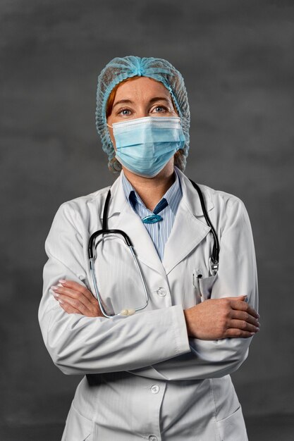 Vista frontal de la doctora con máscara médica y redecilla posando con los brazos cruzados