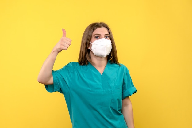 Foto gratuita vista frontal de la doctora con máscara en pared amarilla