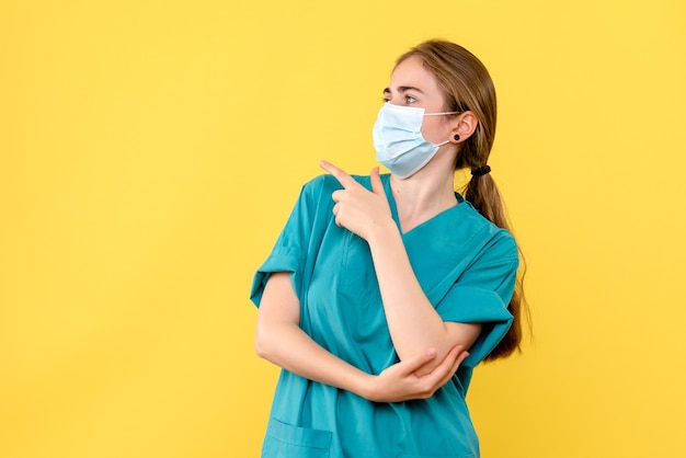 Vista frontal doctora en máscara sobre fondo amarillo covid- pandemia de salud hospitalaria
