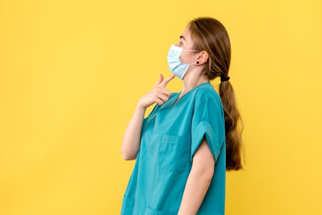 Vista frontal doctora en máscara sobre fondo amarillo covid pandémico del hospital de salud