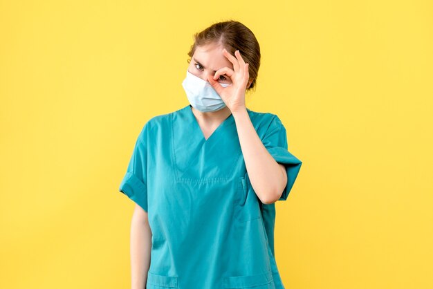 Vista frontal doctora en máscara sobre fondo amarillo pandemia de covid del hospital de salud