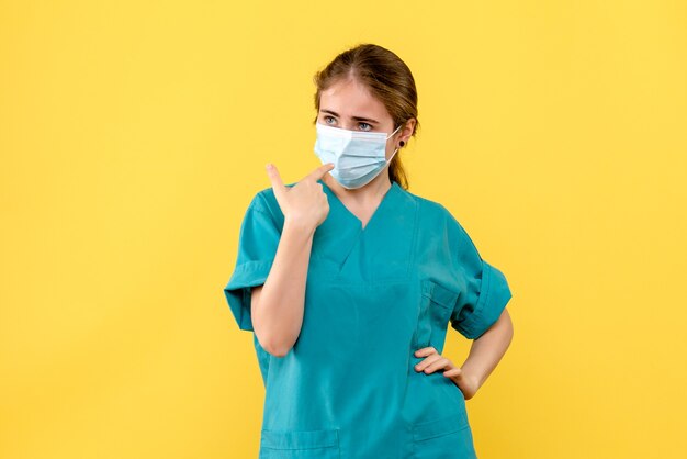 Vista frontal doctora en máscara sobre fondo amarillo virus de salud pandémica covid