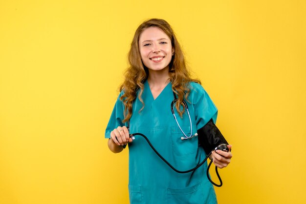 Vista frontal de la doctora midiendo la presión en la pared amarilla