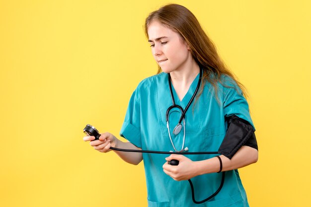 Vista frontal doctora midiendo la presión sobre fondo amarillo claro médico del hospital de salud