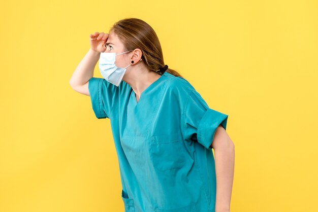 Vista frontal doctora mirando a distancia sobre fondo amarillo virus de salud covid pandémico