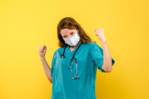 Vista frontal de la doctora regocijándose en máscara en pared amarilla