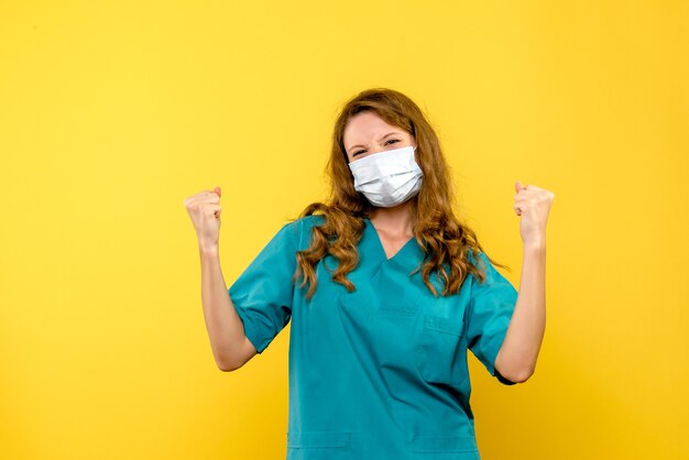 Vista frontal de la doctora regocijándose en máscara en pared amarilla