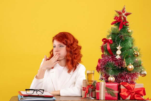 Vista frontal doctora sentada detrás de la mesa con regalos de navidad en amarillo