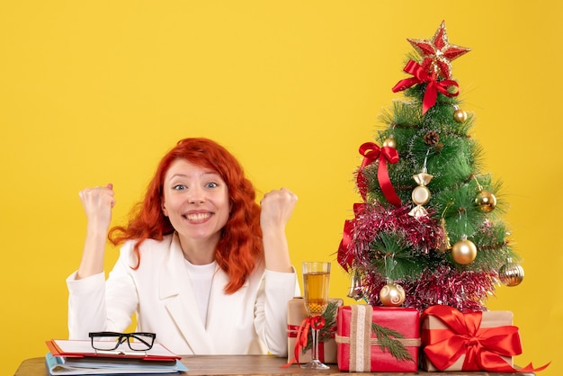 Vista frontal doctora sentada detrás de la mesa con regalos de navidad en amarillo