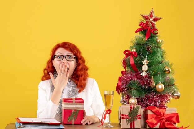 Vista frontal doctora sentada detrás de la mesa con regalos de navidad en el escritorio amarillo