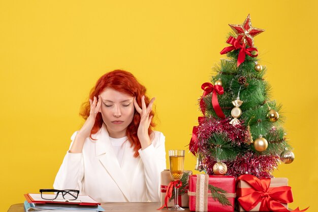 Vista frontal doctora sentada detrás de la mesa con regalos de navidad en el escritorio amarillo