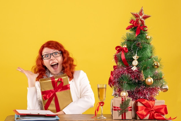 Vista frontal doctora sentada con regalos de Navidad sobre fondo amarillo