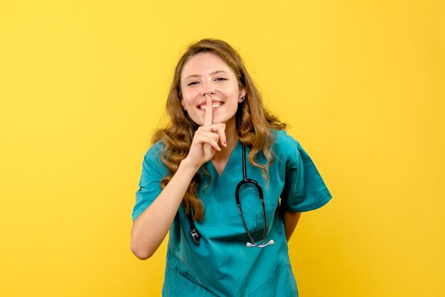 Vista frontal de la doctora sonriendo en la pared amarilla