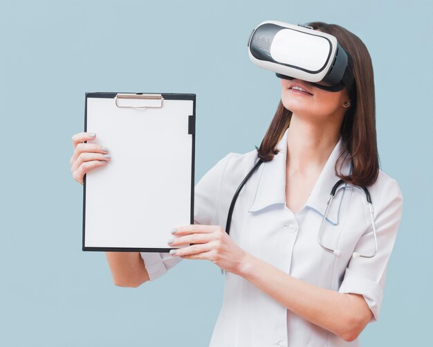 Vista frontal de la doctora sosteniendo el bloc de notas mientras usa casco de realidad virtual