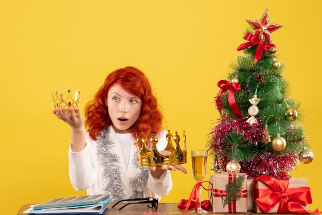 Vista frontal doctora sosteniendo coronas alrededor del árbol de Navidad y regalos