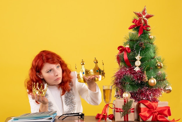 Vista frontal doctora sosteniendo coronas alrededor del árbol de Navidad y regalos